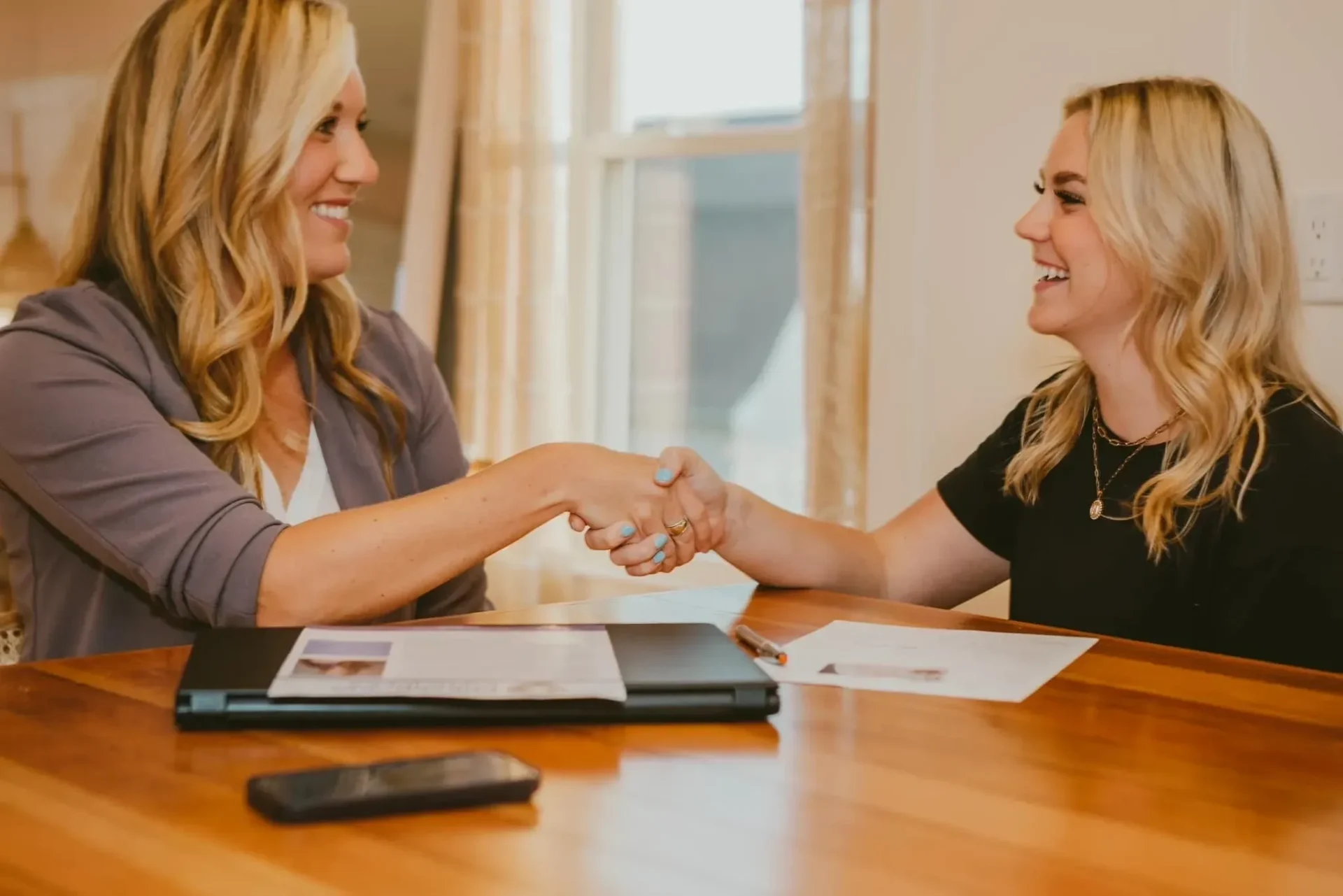 Two women shaking hands over a wooden table.