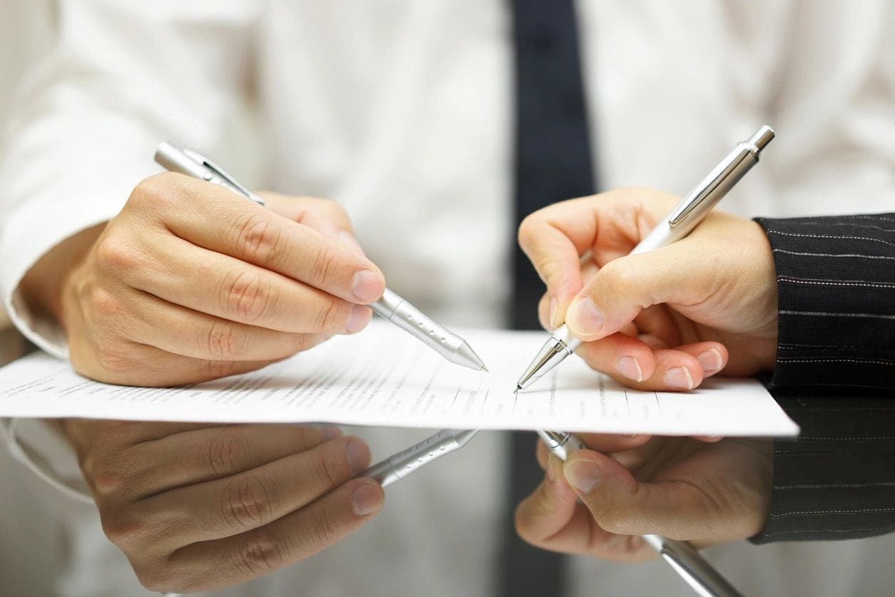 Two people are writing on a piece of paper.