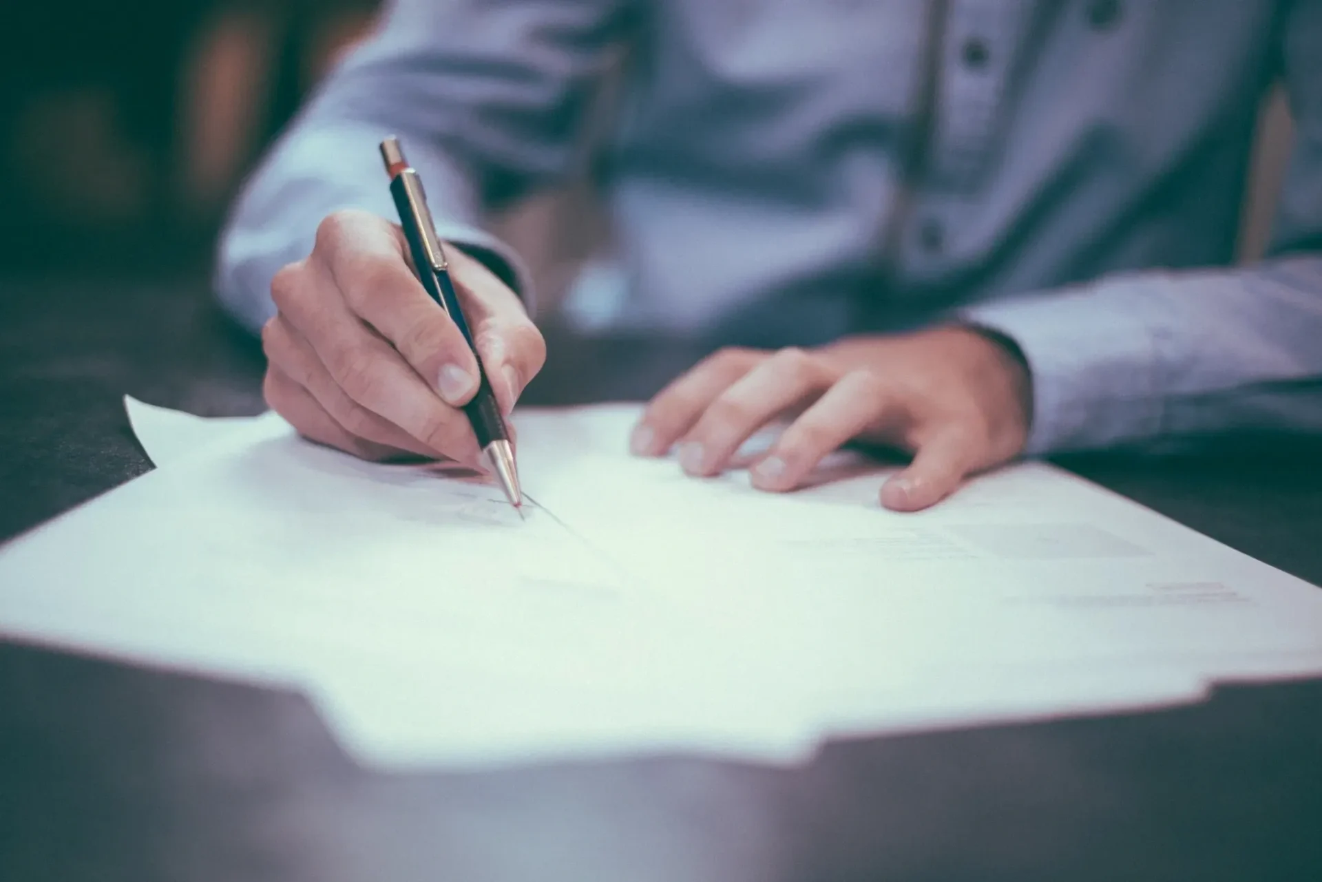 A person writing on paper with a pen and pencil.